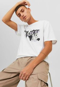 Camiseta blanca de manga corta con un estampado gráfico en negro y morado que incluye texto. Fabricada en un material de algodón suave, con un corte relajado y escote redondo.