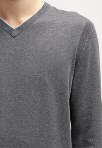 Grå V-ringad tröja i mjukt, strukturerat stickat material. Har ribbat halsringning och muddar, med en figurnära siluett.