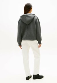 Sweat à capuche gris avec une coupe décontractée et une grande capuche, associé à un pantalon blanc et des bottines noires. Texture lisse avec des poignets côtelés.