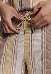 Gestreepte katoenen broek in beige, bruin en geel. Voorzien van een trekkoord met metalen tips. Textuurstof met afwisselend dunne strepen.