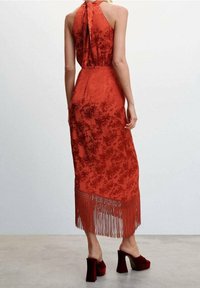 Vestido de patrón floral rojo con cuello halter, dobladillo con flecos y silueta ajustada. Combinado con zapatos de tacón cuadrado rojos.