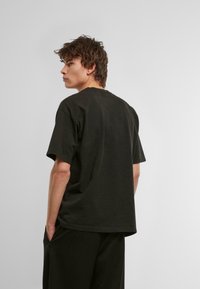 Camiseta de algodón negra con mangas cortas, corte relajado y escote redondo, vista desde la parte posterior con una textura sólida.