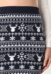 Jupe en tricot navy ornée de motifs de rennes blancs et de flocons de neige, avec une taille côtelée et une texture lisse.