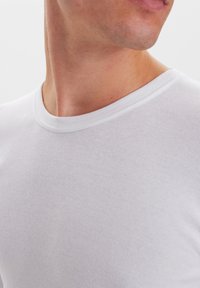 Hvid ribbet bomulds t-shirt med en klassisk rund halsudskæring og tekstureret stof, der fremhæver det tætsiddende design og den glatte finish.