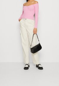 Off-shoulder rosa ribbad stickad topp, krämfärgade vida byxor, svart texturerad handväska och svarta och silverfärgade platåskor med remdetalj.