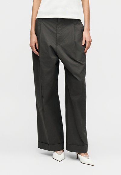 Pantalon gris à jambes larges avec une texture lisse et des détails de plis. Ourlets retroussés, porté avec des talons blancs à bout pointu.