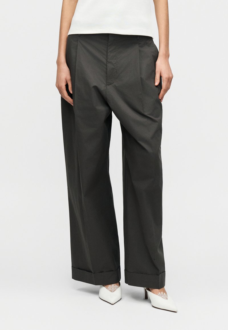 Γκρι παντελόνι με φαρδιά μπατζάκια, λείο ύφασμα και πιέτες. Ρεβέρ στα τελειώματα και συνδυασμένο με λευκές γόβες μυτερές.