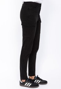 Zwarte cargobroek met zijzakken, slim fit, gemaakt van een katoenmix. Gecombineerd met zwarte sneakers met witte strepen.