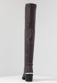 Bota gris de ante por encima de la rodilla con acabado texturizado, punta redonda y tacón bloque moderado, con un detalle plateado brillante en el talón.