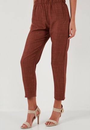 Eisenfarbene, taillierte Hose mit bequemem Schnitt, elastischem Bund, Seitentaschen und strukturierter Oberfläche, kombiniert mit beigen High-Heels.