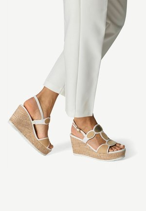 Sandali con zeppa bianchi con dettagli circolari e suede color cuoio, caratterizzati da una texture intrecciata sulla suola e un design con cinturino alla caviglia.