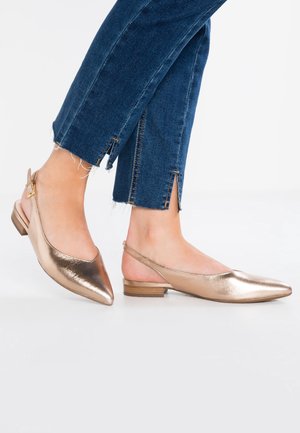 Kvinder fødder iført metallic spidse slingback flade sko kombineret med blå korte jeans med små sideslids ved anklerne.