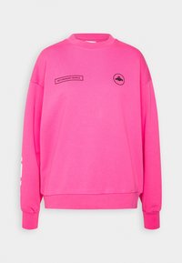 Sudadera rosa con cuello redondo, mangas largas y un corte rectangular. Presenta texto negro y gráficos en la parte delantera y en la manga.