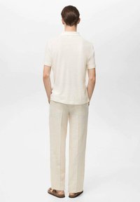 Polo a maniche corte in tessuto crema abbinato a pantaloni in lino beige chiaro e sandali marroni, caratterizzato da un design semplice e pulito.
