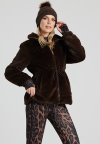Brun fuskpäls zip-up jacka med dragsko i midjan, i kombination med brun och svart leopardmönstrade leggings. Stickad mössa med pom-pom detalj.