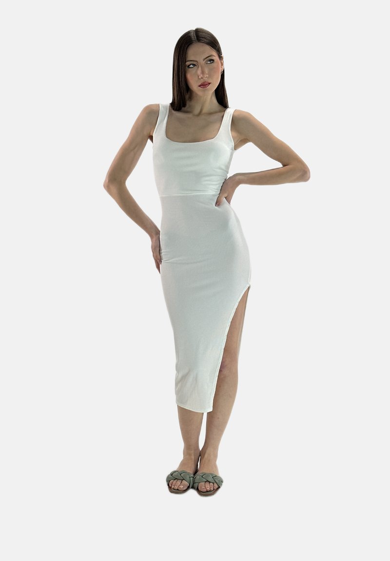 Vestido midi ajustado blanco con escote cuadrado, textura acanalada y abertura lateral hasta el muslo, combinado con sandalias verdes. 