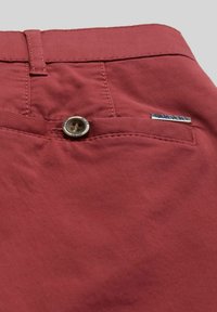 Rode katoenen broek met een knoopsluiting en een klein metalen logobadge. Soepele textuur met een enkele voorkennis.