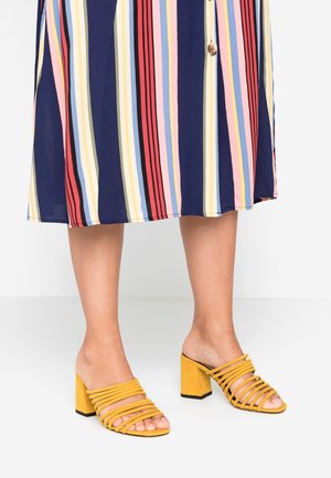 Żółte zamszowe sandały na płaskiej podeszwie z wielokolorowym paskowym wzorem, z szerokimi poziomymi paskami, otwartym noskiem i grubym czarnym obcasem.