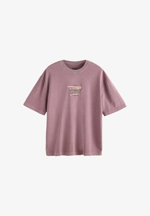 Lilla toonides liibuv T-särk lühikeste varrukatega, ümar kaelus ning väike tuhmunud graafiline tekst ja disain rinnal keskel.