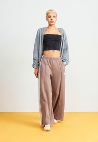 Sudadera gris con cremallera sobre un top negro corto y pantalones anchos color marrón claro con rayas blancas. La modelo lleva zapatillas blancas.
