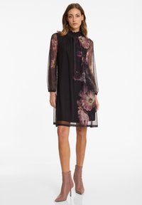 Zwarte jurk met een doorschijnende bloemenoverlay, gerimpelde halslijn en lange mouwen. Gecombineerd met blush enkellaarsjes met een rits.