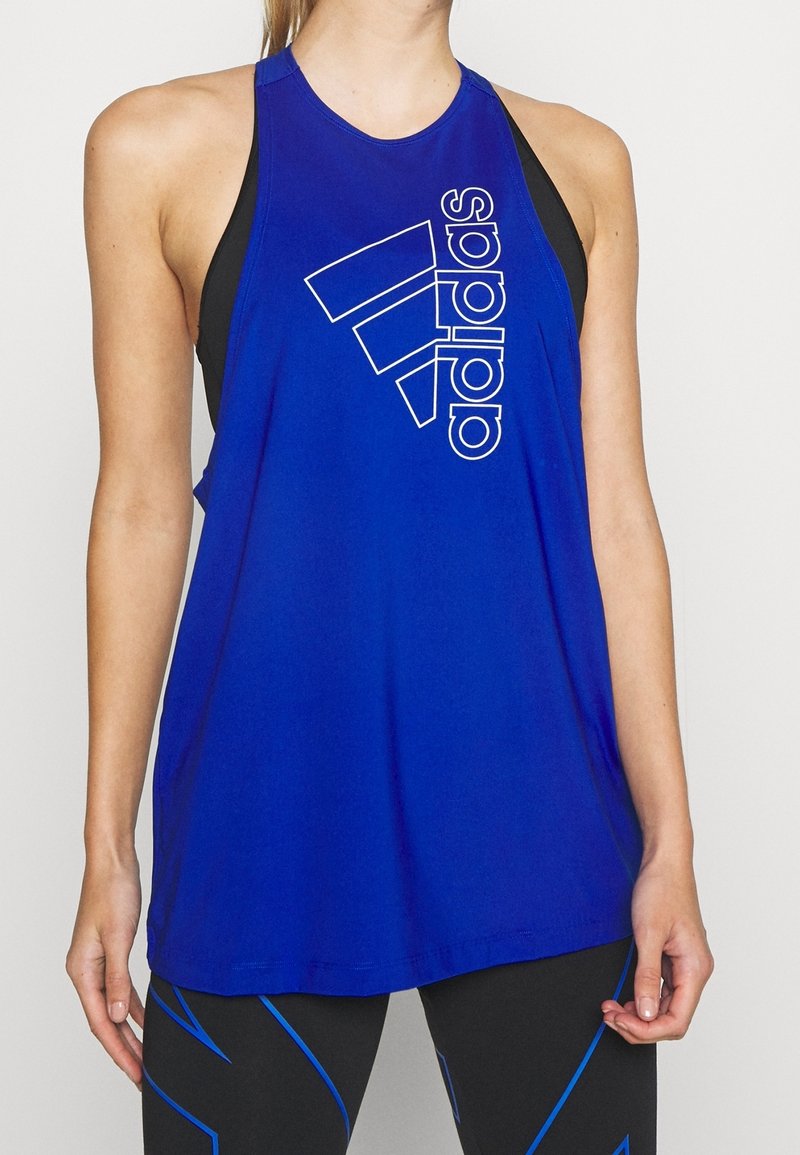 Femme portant un haut sans manches bleu Adidas avec un logo Adidas blanc, associé à des leggings noirs ornés de lignes abstraites bleues.