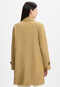 Khaki trench coat with a back vent, raglan sleeves, and buttoned cuffs. Smooth texture and clean lines, designed for a relaxed fit.