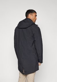 Parka negra con capucha y corte recto, fabricada con un material resistente al agua. Presenta una abertura en la parte posterior y acentos de diseño minimalista.