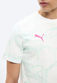 Άνδρας που φοράει λευκό πουκάμισο με κοντό μανίκι, με μοτίβο ελαφρού πράσινου καβούκι και ροζ λογότυπο Puma στο αριστερό στήθος.