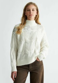 Maglione bianco lavorato a maglia con colletto alto, caratterizzato da un motivo a trecce e dettagli in paillettes sulla spalla sinistra. Polsini e orlo a coste.