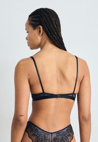 Μαύρο σουτιέν με λεπτές τιράντες, διχτυωτές λεπτομέρειες και κλείσιμο με γάντζο. Η δαντελένια ύφασμα παρουσιάζει μοτίβο πεταλούδας και ψηλή κοπή.