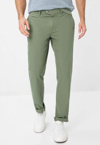 Chinos verdi in cotone con taglio dritto, caratterizzati da chiusura a bottoni, tasche laterali e orli arrotolati, abbinati a sneaker bianche.