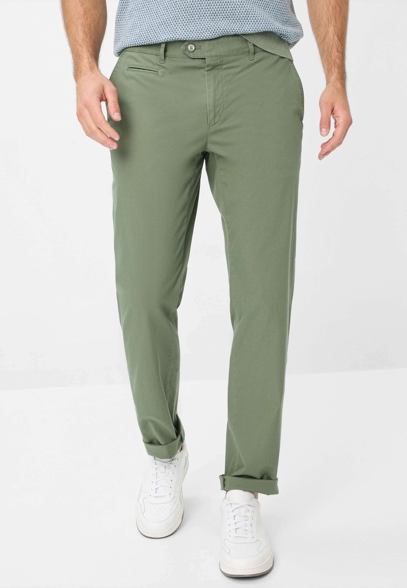 Chinos verdi in cotone con taglio dritto, caratterizzati da chiusura a bottoni, tasche laterali e orli arrotolati, abbinati a sneaker bianche.