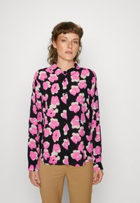 Langarmbluse in Schwarz mit einem leuchtend rosa-weißen Blumenmuster. Weicher Stoff, Knopfverschluss vorne und klassischer Kragen.