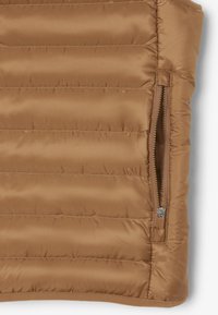 Tan puffer vest met verticale quiltstructuur, een zijrits en een gladde, glanzende textuur. De stof is lichtgewicht en geïsoleerd.