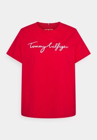 Rød bomulds-T-shirt med et hvidt scriptet "Tommy Hilfiger" logo på brystet. Rund hals, korte ærmer og afslappet pasform.