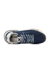 Zapatilla azul marino con parte superior de ante y malla, cordones azul claro, acentos en blanco y gris, y suela de goma. Logo visible en la lengüeta.