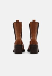 Bottines en cuir marron avec des panneaux latéraux en élastique, talons bloc empilés et languettes à l'arrière. Texture lisse avec un éclat subtil.