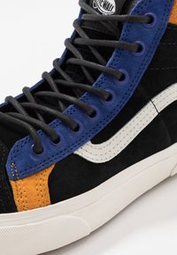 Zwarte suède high-top sneaker met blauwe en oranje accenten. Voorzien van een wit logo en oogjes met zwarte veters en een gestructureerde rubberen zool.