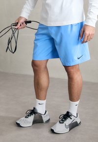 Heledad helesinine spordipüks, millel on must Nike logo, koos hallide ja mustade tenniste ning valgete soonikkoes sokkidega. Käes hüppelnöör.