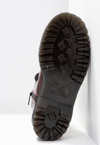 Semelle d'une botte beige foncé avec des crampons profonds et une fermeture éclair sur le côté, présentée sur un fond blanc en coin.