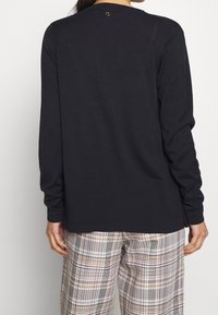 Marinblå stickad tröja med långa ärmar och ribbat avslut, med en liten logotyp på baksidan av kragen, kombinerad med rutiga byxor.