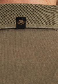 Olivenfarvet skjorte med en tekstureret strikkrave, glat stof på kroppen og et sort mærke med guld "PME LEGEND" branding.