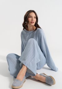 Jasnoniebieski lniany zestaw składający się z dwóch elementów, z długimi rękawami i szerokimi spodniami, w połączeniu z dopasowanymi jasnoniebieskimi espadrylami z jucianą podeszwą.