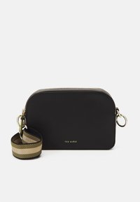 Borsa a mano nera in pelle con hardware dorato, forma rotonda, chiusura con cerniera e tracolla in tessuto a righe con il nome del marchio.