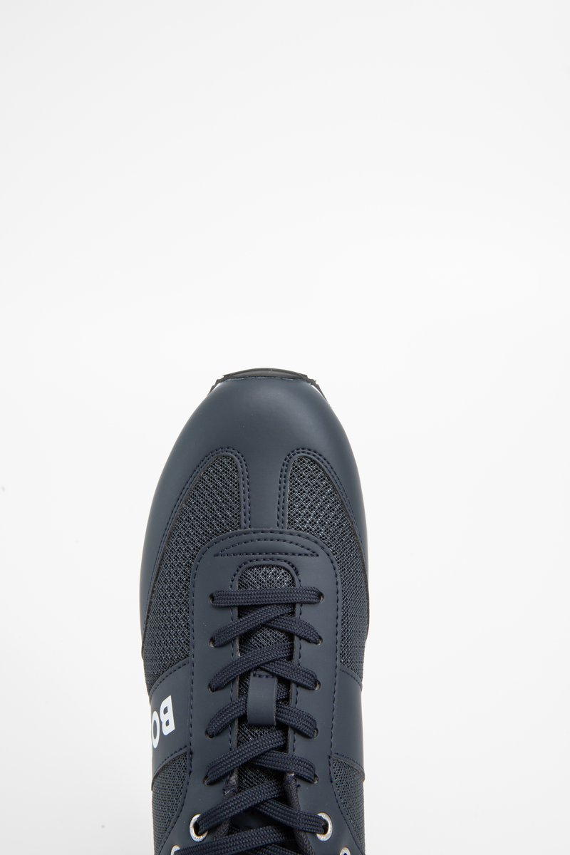 Marineblaue Sneaker mit Mesh-Details, schwarzen Schnürsenkeln und teilweise weißem Markentext an der Seite, von oben auf einem weißen Hintergrund gezeigt.