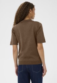 Barna, rövid ujjú golfpóló, facsípő gallérral és szegélyezéssel; sima textúrával és testhezálló fazonban, kék farmernadrággal párosítva, hátulról nézve.