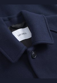 Navy wool coat featuring a broad collar, black button closure, and an inner lining with a label reading "LES DEUX." Soft texture and tailored design.