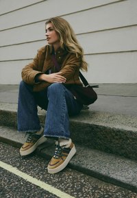 Beige und braune Plateausneaker aus strukturiertem Stoff, mit Schnürdesign und Kunstfellfutter. Getragen mit blauen Schlagjeans und einer braunen Steppjacke.