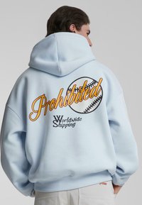 Felpa con cappuccio di colore blu chiaro con grande testo "Proibito" giallo e nero e grafica di baseball sul retro. Polsini e orlo a costine.